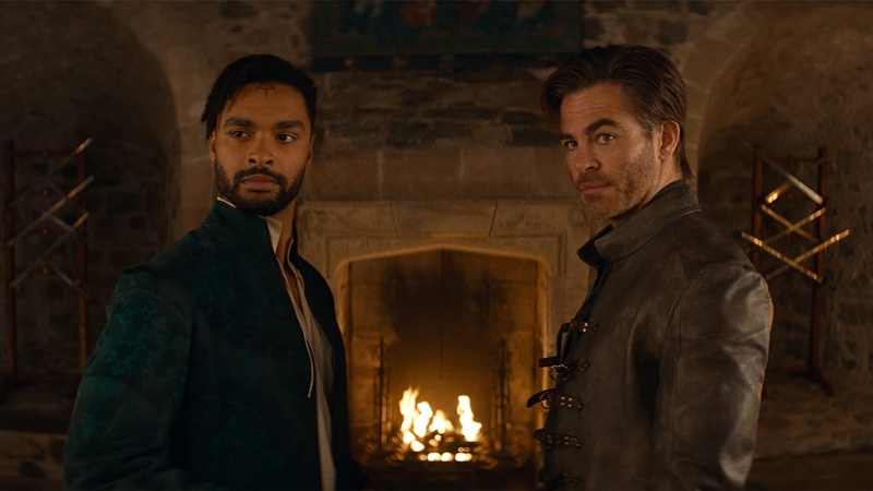 A shot from “Dungeons & Dragons” film. Two characters from the film, Xenk Yendar and Edgin Darvis, are standing in a cosy room with a fireplace. They’re faces are focused, as if they were listening to someone.